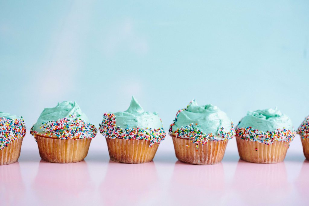 There is a row of 4 cup cakes with blue icing and sprinkles.